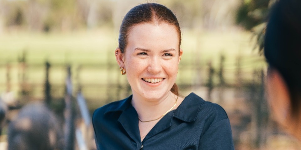 A smiling vet student holds onto a fence railing.