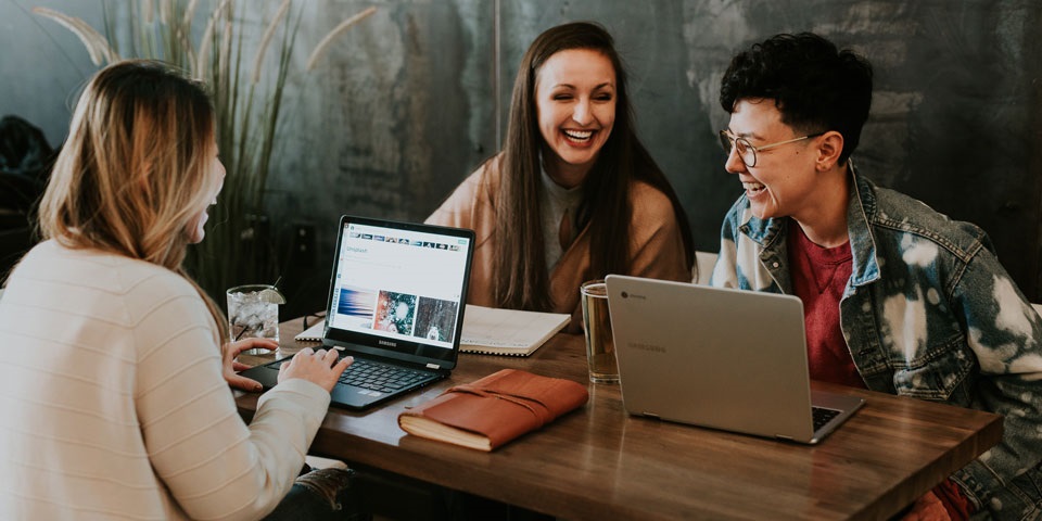 Three women working on laptops at a table, focused and engaged in their tasks.