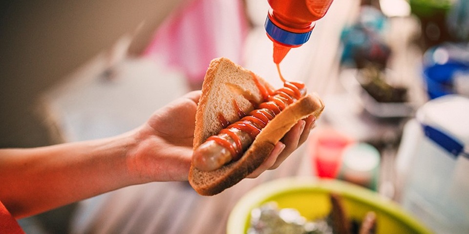 5 Aussie Things To Try Feature Image of person's hand holding piece of bread with barbecued sausage