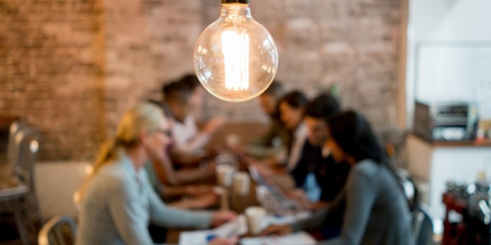 A group of people collaborating underneath a light bulb
