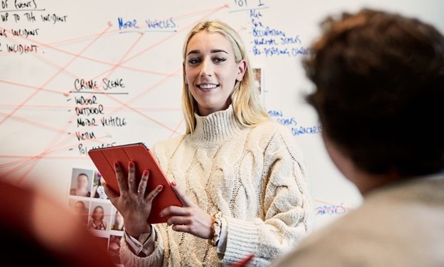 Student stands in front of whiteboard holding a clipboard