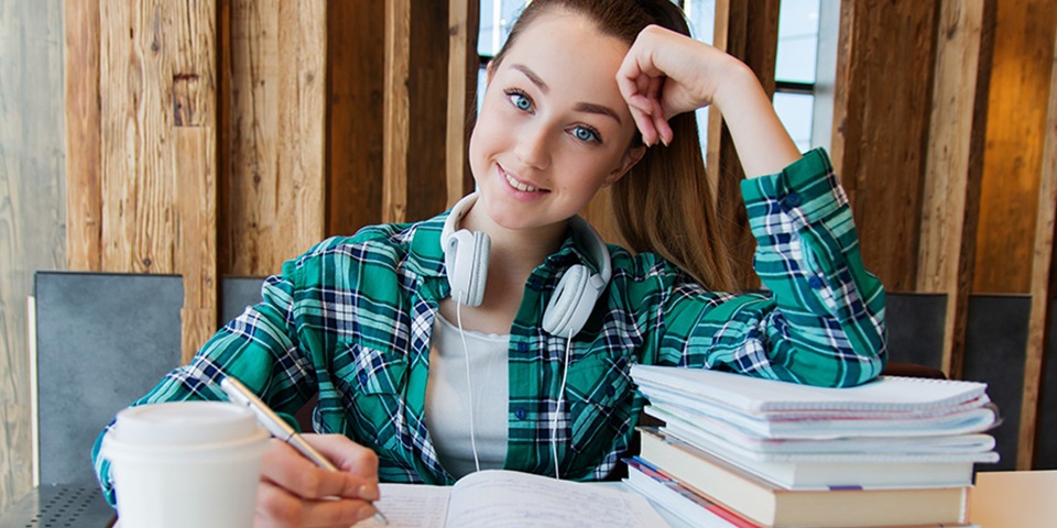 Academic pressure feature Young girl sitting at desk with notebook, books, and coffee