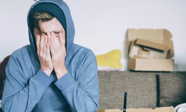 man in blue hoodie with his face in his hands