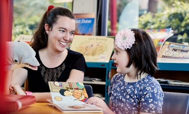 Student reads a book with a child in a classroom