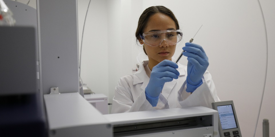 Female scientist wearing white lab coat taking sample from test tube with a syringe