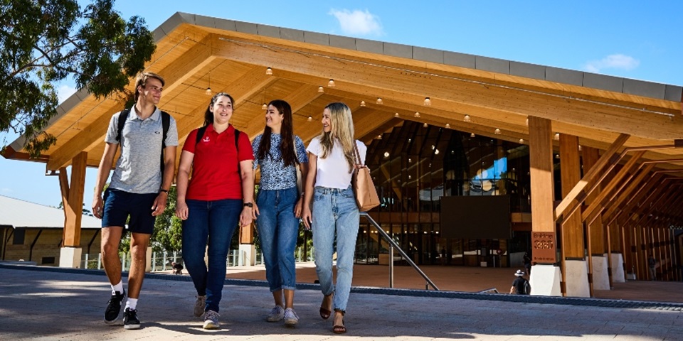 Brighter Futures Scholarships Four students walking toward the camera, talking and smiling, with large timber building in the background