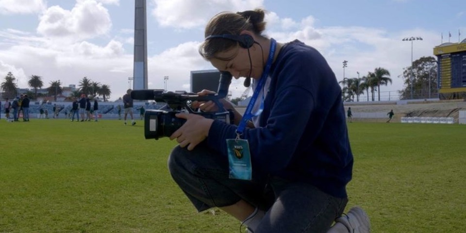 Student looks through video camera on a sports field