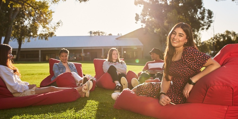 Girl turned to camera smiling, sitting among a group of students sitting on beanbags an grass