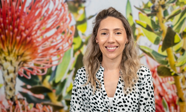 Dr Bep Uink smiling at camera in front of large print of red grevillea