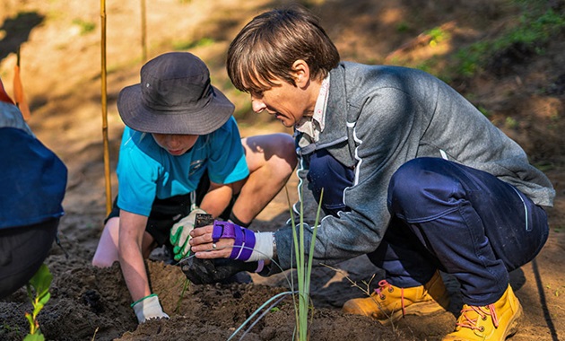 Woman and primary school student crouched on the ground planting tubestock