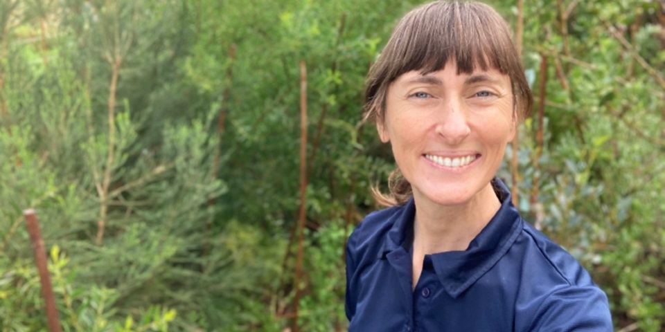 Woman smiling at camera in front of a bushy garden