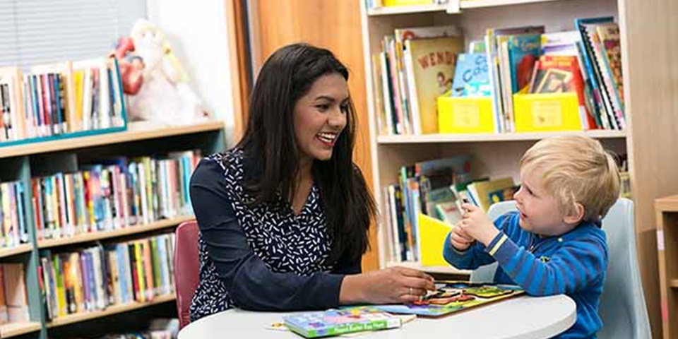 education-study-thumbnail Teacher sits with early childhood student in library.