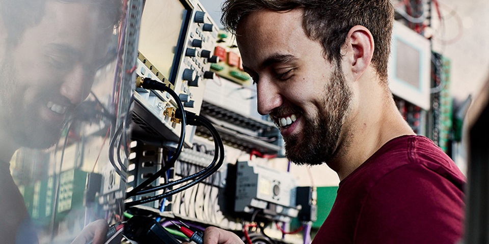 Engineering_Job_Feature Smiling man works on switchboard.