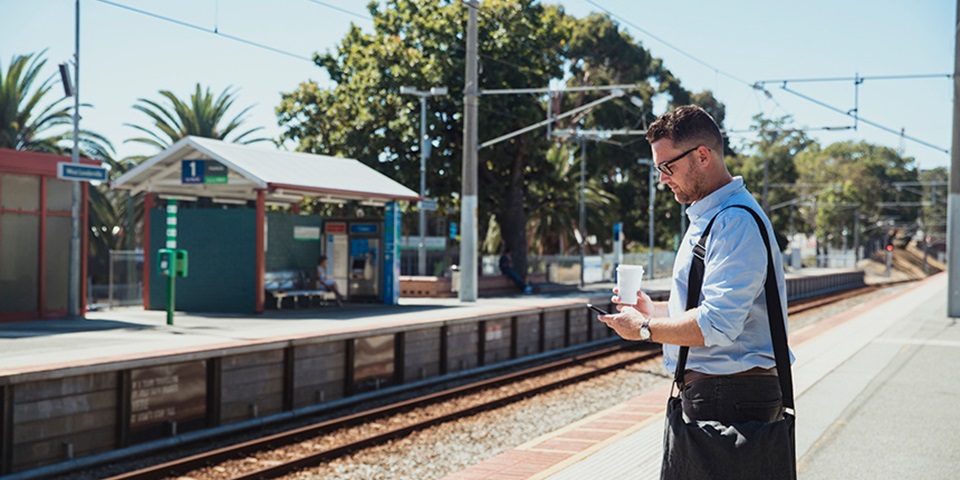 Getting around Perth feature image Man with a bag and coffee waiting at a Perth train station