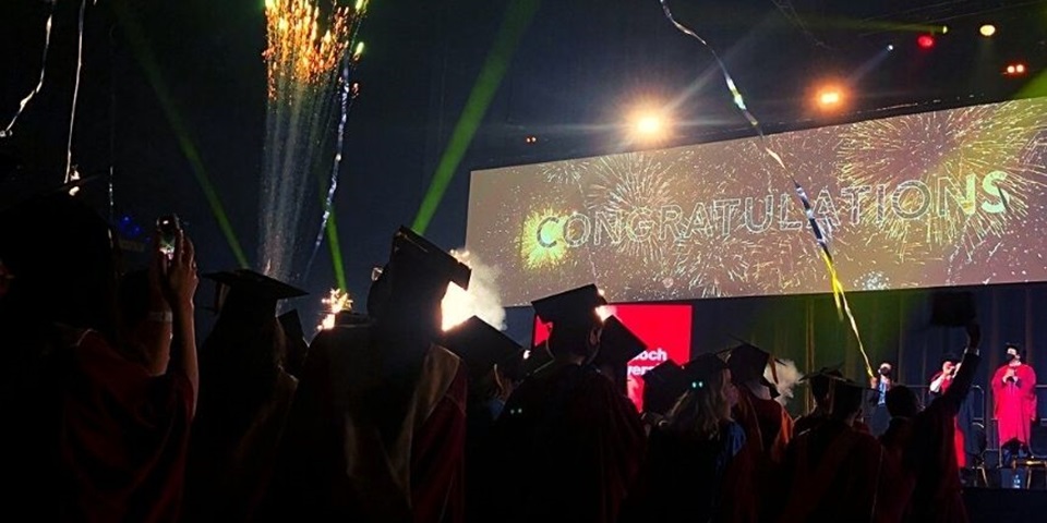 Graduates at ceremony with big Congratulations banner in background