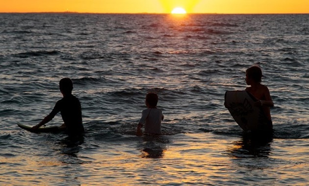 Three young people swimming in the ocean at sunset.