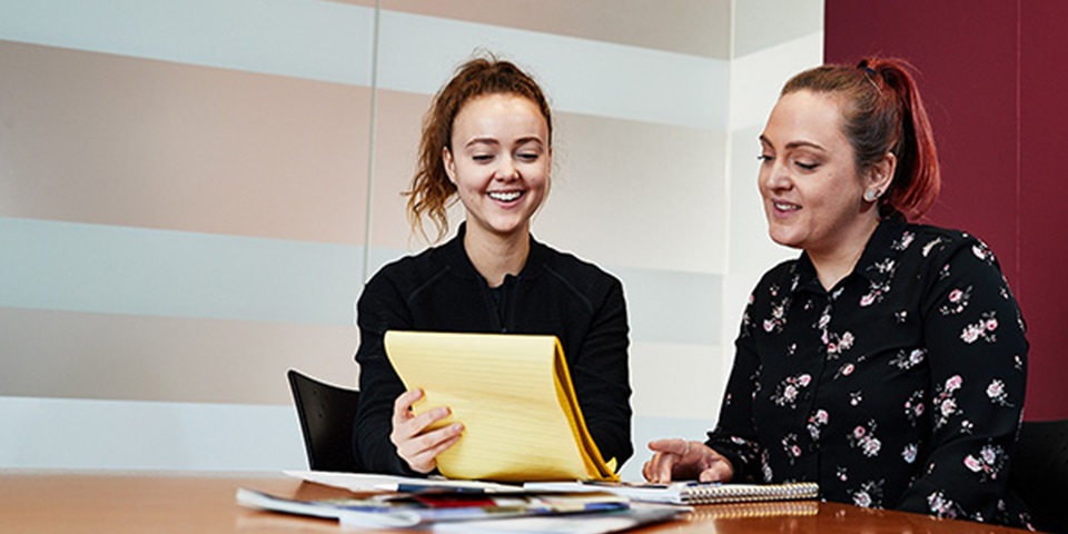 Two women look at a yellow legal pad.