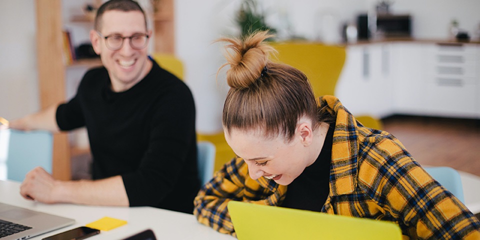 Woman and man laughing at desk with laptops