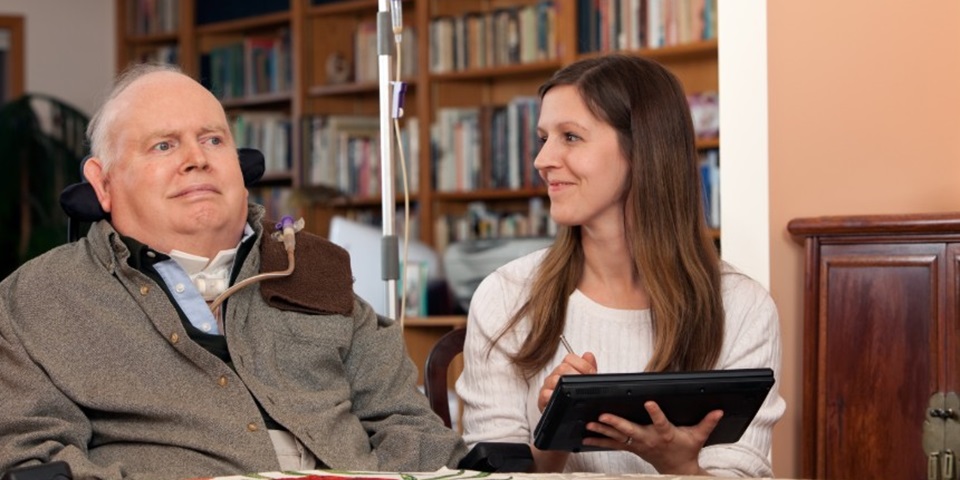 home heathcare nurse, who is working on electronic charting, exchanges a smile with her patient.
