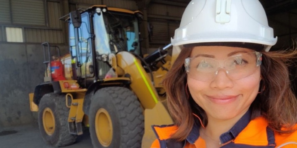 Pauline - Feature Pauline standing in hi-vis in front of a digger
