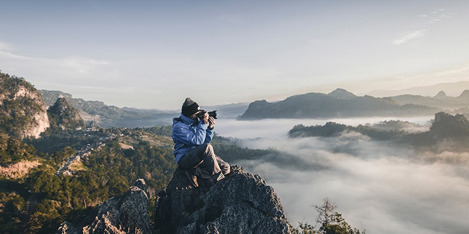 Photographer at the top of a mountain Man taking a photo at the top of a misty mountain range