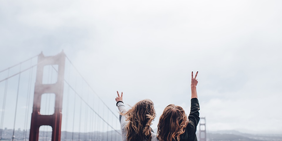 Two girls waving their hand in the air in front of bridge