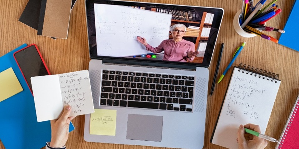 A student watching an online lecture and taking notes