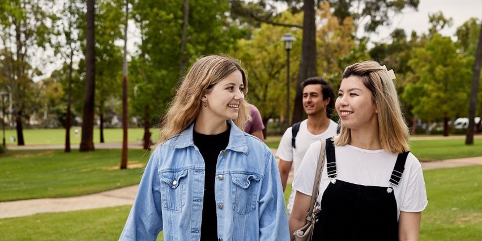TAFE to Uni Feature Two students walking on campus smiling at each other