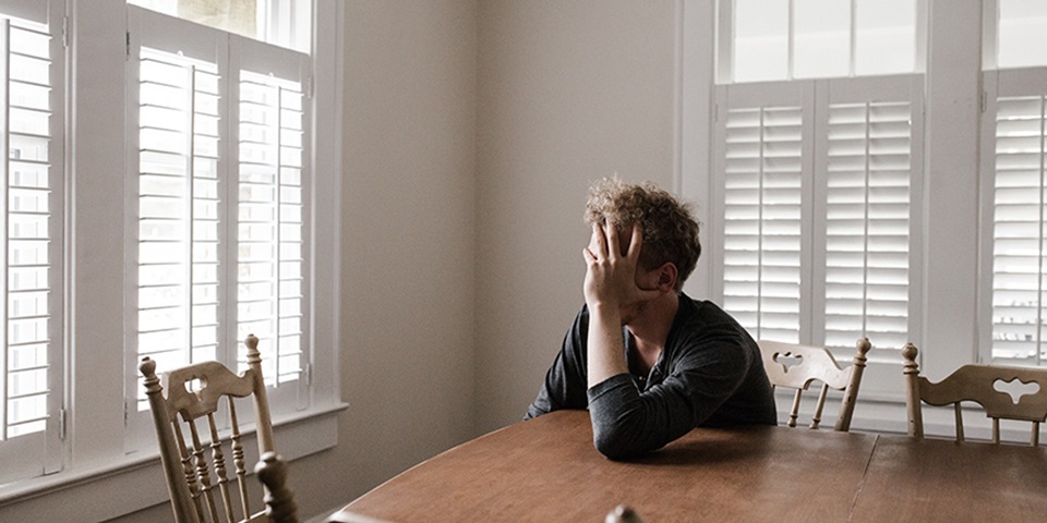Teenage boy sitting with head in head at table feature Teenage boy sitting with head in head at table