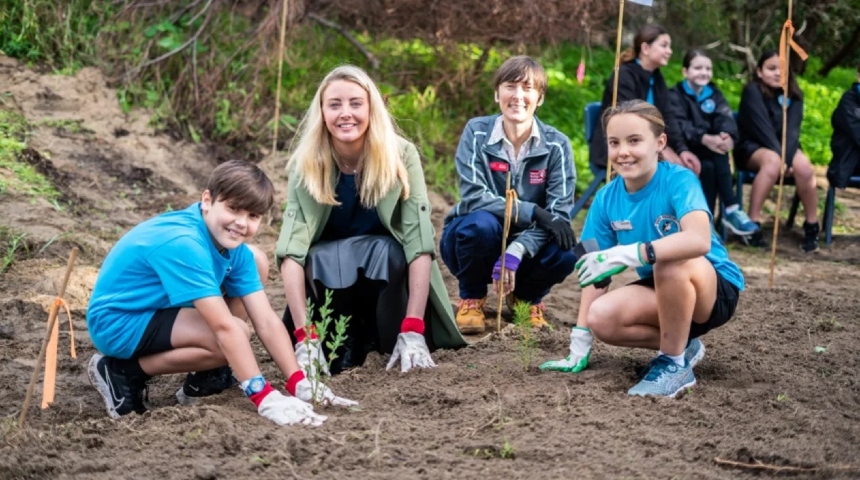 Two women and two children planting a seedlings in an open space