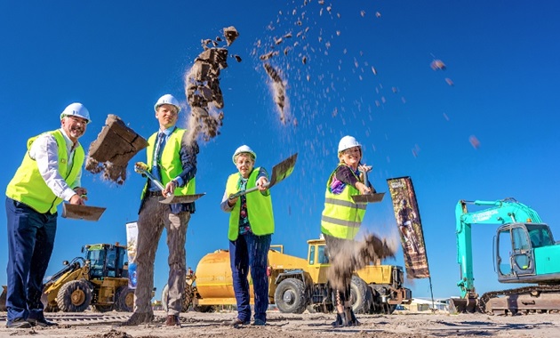 Four people throwing soil from spades at construction site of new food facility