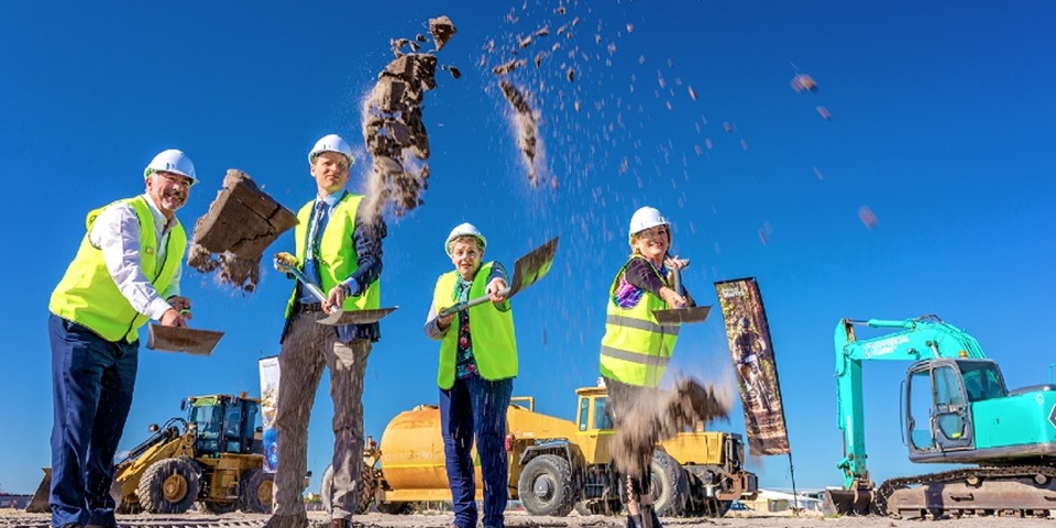 Four people throwing soil from spades at construction site of new food facility