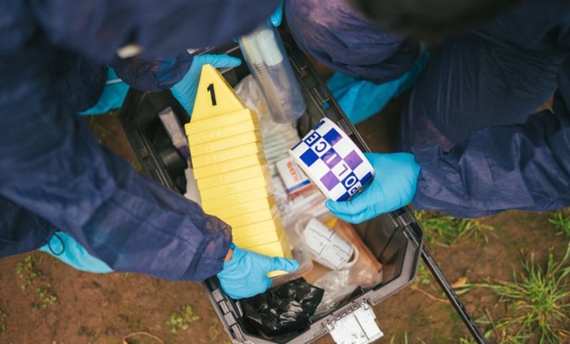 Two people in forensic gear taking tape and markers from a box.