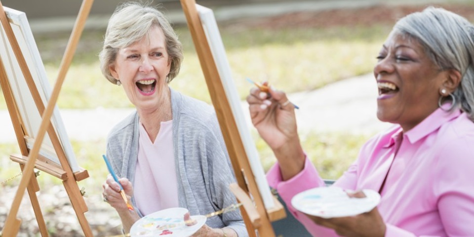 Two senior women laughing and painting