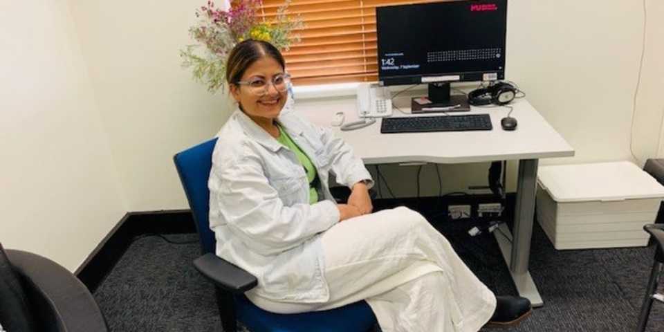 Student in lab coat sits in front of computer smiling