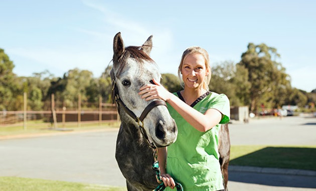 Female student standing next to a horse, smiling.