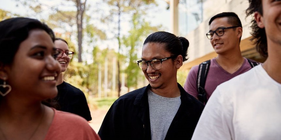 What is HECS-HELP? Feature image 860x480 Close up of group of students walking through campus, student in middle is in focus and is smiling off camera